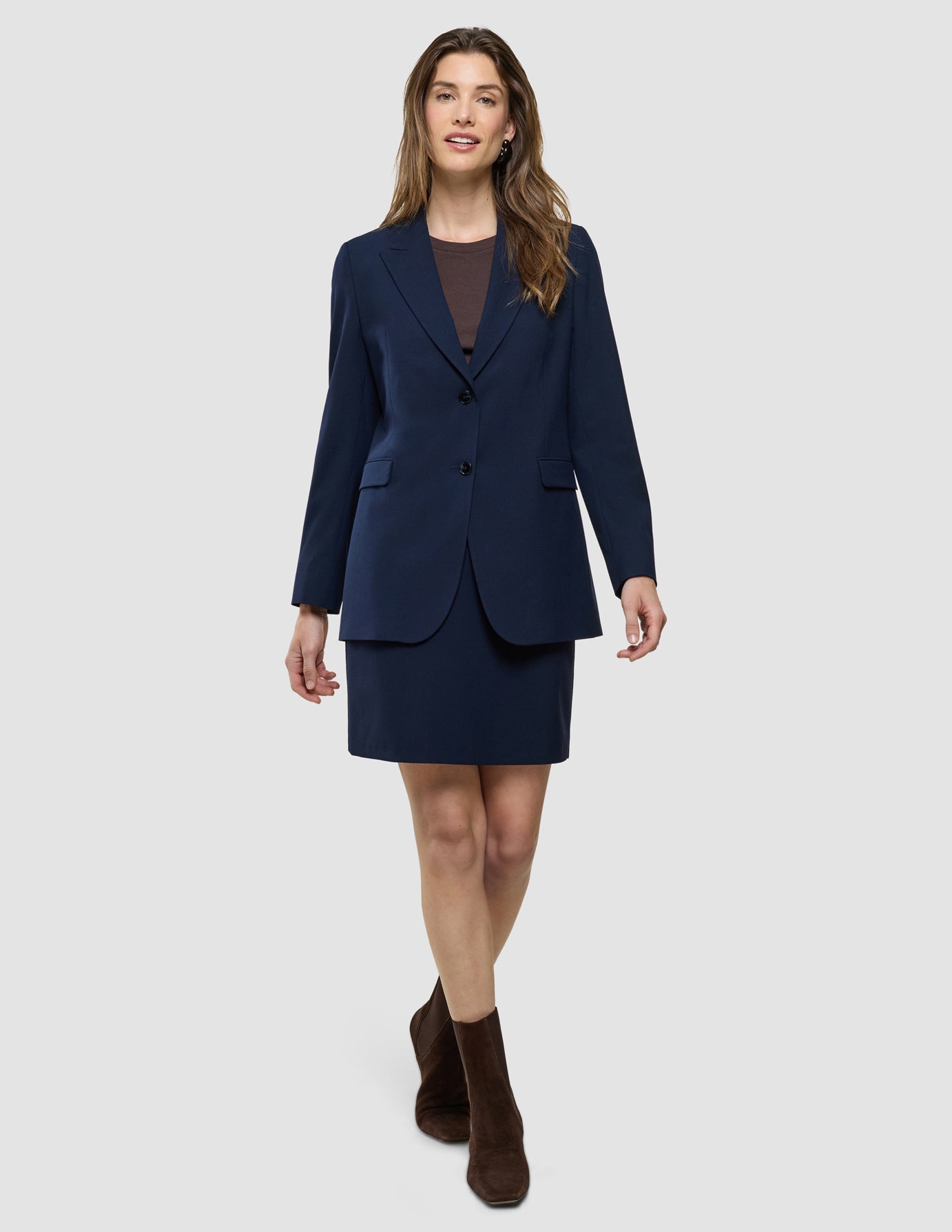 En kvinna klädd i en marinblå kavaj, en kort kjol från Women Ease i färgen ”Blue Nights”, en brun topp och ankelstövlar.